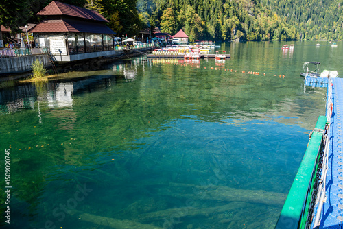 Gaga district, Abkhazia October 12, 2024: Alpine lake Ritsa. Boats sail on smooth turquoise water. Mountain slopes are covered with dense forest. Sunny autumn day