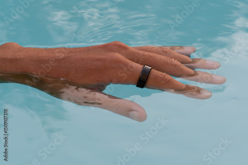 Hand, submerged in clear pool water showcasing a sleek waterproof black smart ring with health tracker.