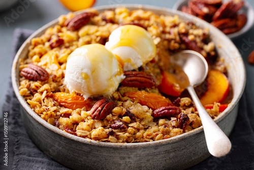 Peach crumble cake with ice cream and pecan nuts in bowl. Grey background. Close up.