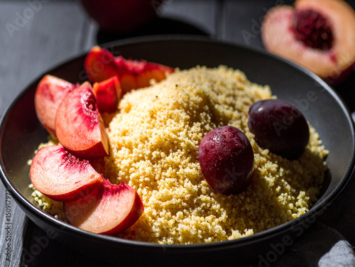 A bowl of millet groats with sliced peaches and red grapes, placed on a wooden table. A suggestion for a healthy breakfast or afternoon snack.
