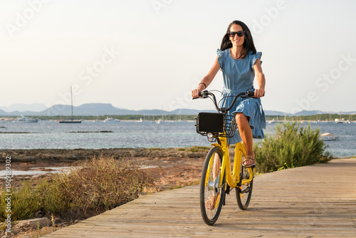 Bild auf Leinwand Cheerful woman riding bicycle along embankment near sea