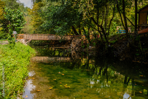 Fototapeta Naklejka Na Ścianę i Meble -  Tranquil Creek with Wooden Footbridge Surrounded by Lush Greenery in Başiskele, Kocaeli, Türkiye on a Sunny Day