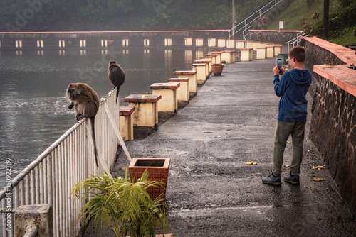 Beautiful view of a young boy taking a photo of macaques taking over the promenade along the banks of the Grand Bassin Hindu temple in Mauritius