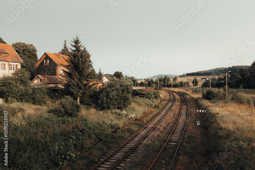 Fototapeta Naklejka Na Ścianę i Meble -  Picturesque railway tracks leading through a rural landscape with houses and trees in the background, on a sunny day