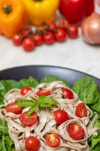 Wholemeal pasta with green leaves of arugula and Cherry tomato on black plate and white marble background