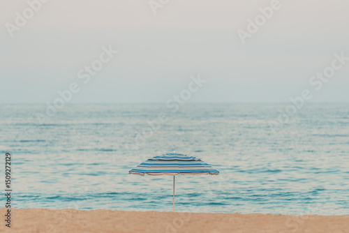 Fototapeta Naklejka Na Ścianę i Meble -  Lonely sun umbrella parasol at sandy beach on overcast summer day