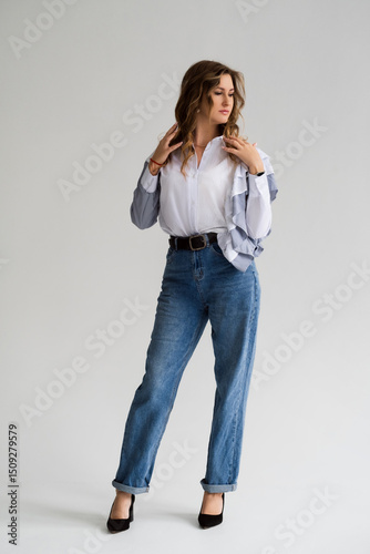 Photo of a smiling young woman, wearing a white shirt and jeans. Young businesswoman with the curls looking sideways