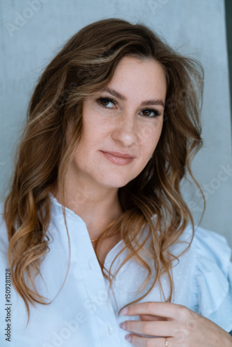 Portrait of a smiling young woman, wearing a white shirt. Young businesswoman with the curls looks at camera