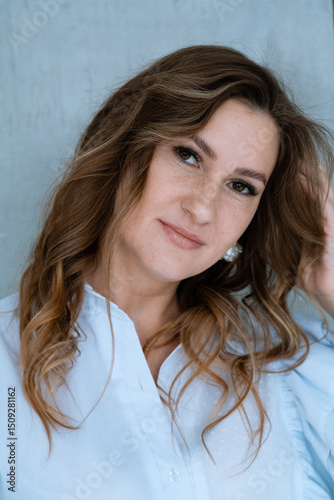 Portrait of a smiling young woman, wearing a white shirt. Young businesswoman with the curls looks at camera