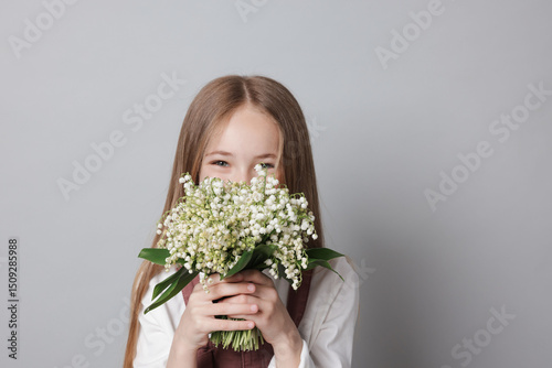 Girl with bouquet of beautiful lily-of-the-valley flowers on light grey background