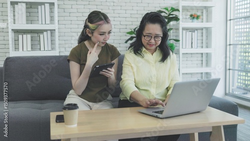 Asian mother and daughter working together on laptop and tablet at home