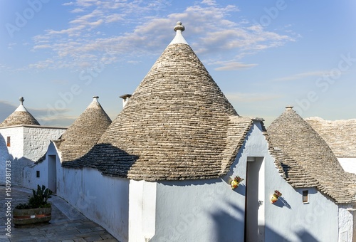 Fototapeta Naklejka Na Ścianę i Meble -  old mediterranean town with old beautiful houses with white walls and pretty tile roofs with  narrow vintage streets and amazing sky on background. Buildings of trulli in Alberobello, Italy.