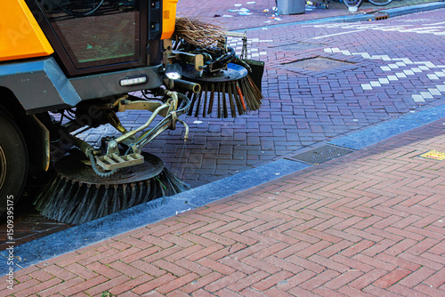 Urban maintenance vehicle cleaning brick pavement using rotating brushes and water spray.