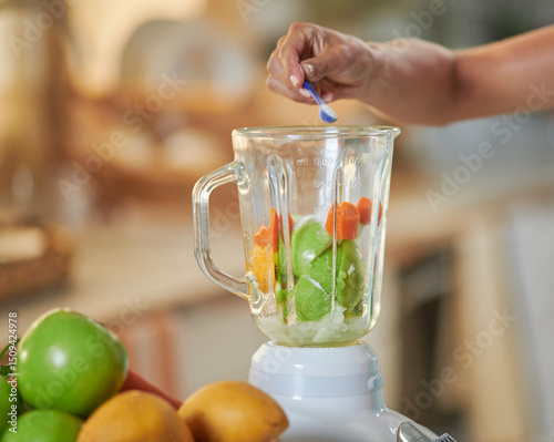 Manos de mujer con camisa azul  sirviendo  endulzante  en una licuadora para preparar jugo saludable