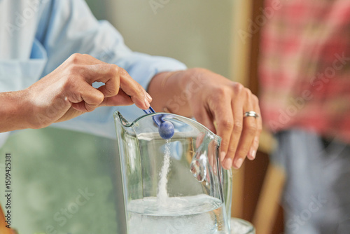 Manos de mujer con camisa azul  sirviendo  endulzante  en una jarra de agua