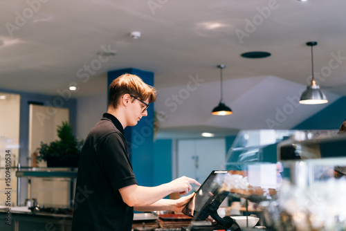 Young waiter serving customer at cash point in cafe. Man working with POS terminal. Student working part-time. Problems of unemployment and Job opportunities for youth. Small business vacancies