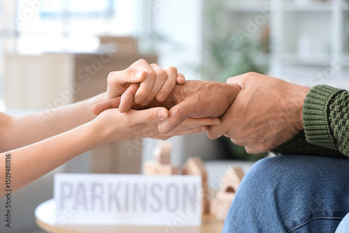 Senior man suffering from Parkinson syndrome with woman holding hands at home, closeup