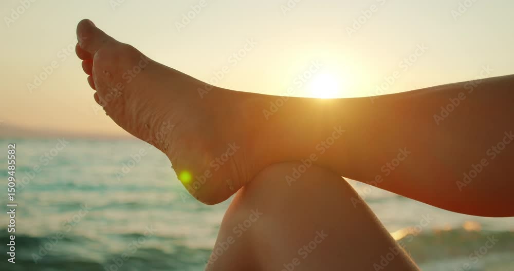Person relaxes on the beach with one leg crossed over the other as the sun sets over the sea Person relaxes on the beach with one leg crossed over the other as the sun sets over the sea