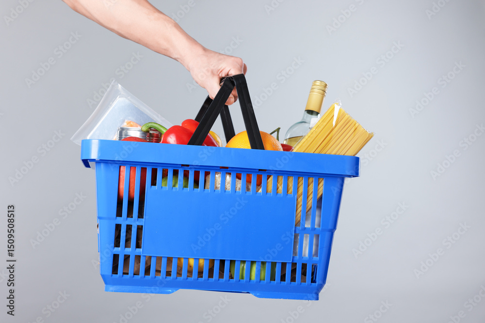 Fototapeta premium Man holding shopping basket with different products on grey background, closeup