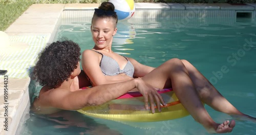 Relaxing in pool, happy diverse couple enjoying sunny day on inflatable float