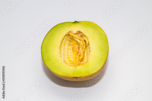 A halved melon, revealing bright green flesh and a central cavity filled with seeds and pulp, on a white background.