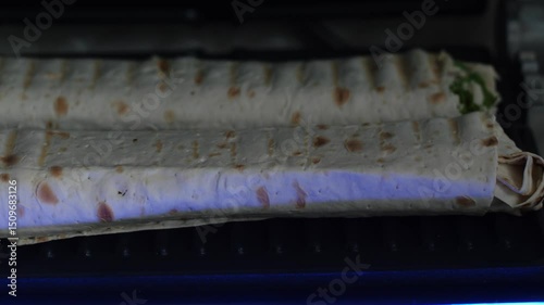 Close-up of a burrito or shawarma being roasted on a griddle stove in a café, emphasizing the appetizing texture and culinary preparation process