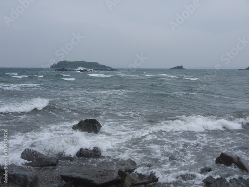 Standing on the rocky sea shore with stormy waves on overcast day