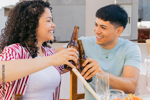 Foto Young Latin man and woman gaze lovingly at each other and toast with beer bottle
