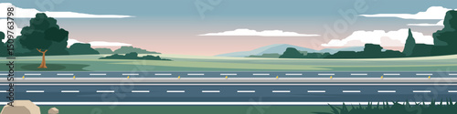 Horizontal or landscape four lane asphalt road. On the wide grassland with grass and trees growing on the side of the road. Soft colors of the mountains and a calm evening sky.
