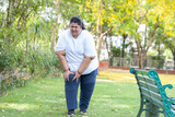 Overweight indian woman suffering from knee pain while walking in summer park .Plus size lady have joint inflammation or injury, Fat people health care and medical concept