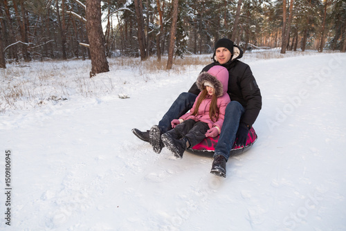 Father and daughter having fun with snow tube in the forest