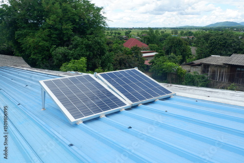 Two large solar panels are installed on a blue metal roof of a rural house using steel legs to support them.