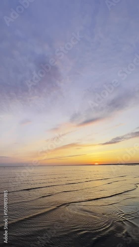 Sea waves rolling on sand beach in golden hour at sunset. Ocean ripples on grey ocean surface at sunrise. Colorful Sunset on seaside. Nature wallpaper. Peaceful natural scene. vertical 9x16 4k.