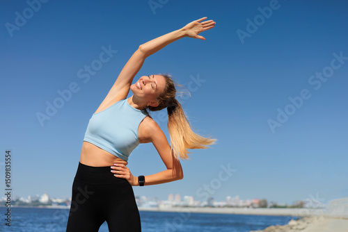 Sport woman fitness stretching body with raising hand at river stone beach back view