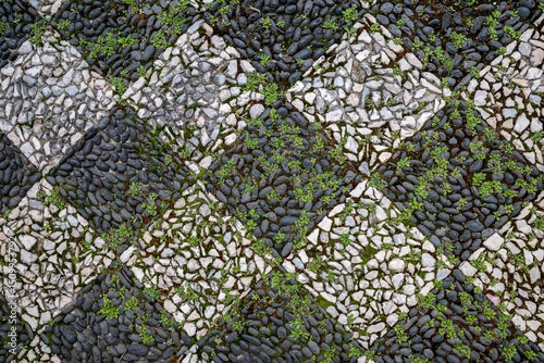 Traditional Portuguese cobblestone pavement features intricate black and white stone mosaic pattern known as calcada portuguesa. Historic geometric square design with basalt and limestone blocks.