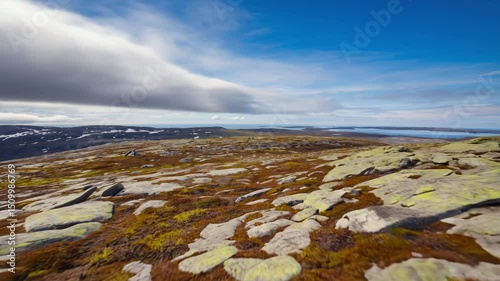 vast nordic tundra landscape with rocky terrain and patches of melting snow under bright blue sky with scattered clouds concept of climate awareness, wilderness travel, environmental storytelling