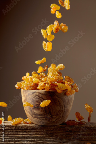 Yellow sultana raisins pour into a wooden bowl.