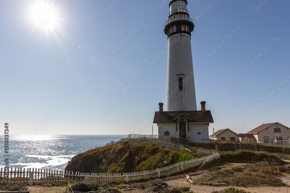 Fototapeta premium A classic California lighthouse stands majestically on rugged cliffs above the Pacific Ocean, bathed in bright sunlight