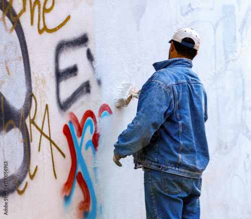 Painter covering graffiti on a public building wall with white paint