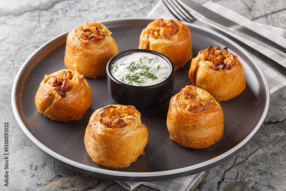Fototapeta premium Ukrainian Knysh are pies with onion and potato filling served with sour cream close-up in a plate on the table. Horizontal