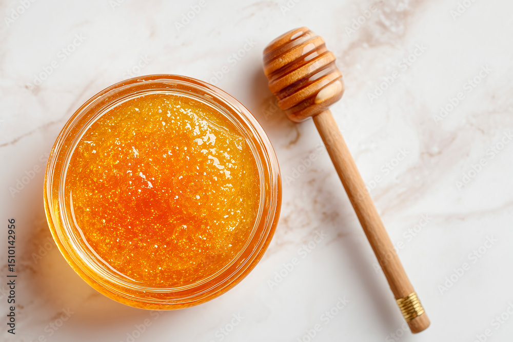 Fototapeta premium A golden honey face mask in a small glass bowl, placed on a white marble background with a honey dipper and a soft brush, viewed from above, evoking a rich and nourishing spa moment