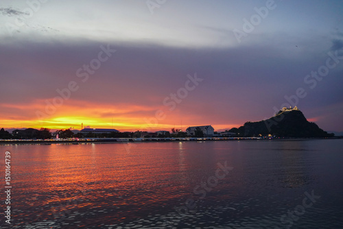 Beautiful view of boats calm water and building with vibrant sky and buildings background, Prachuap bay beach in Prachuap Khiri Khan, Thailand