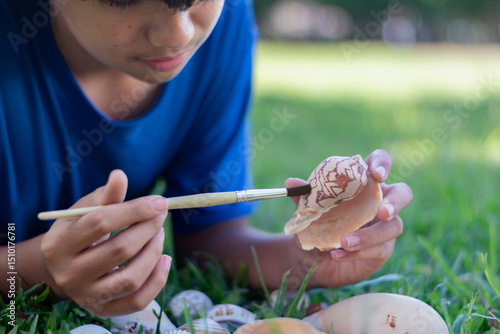 A young boy carefully cleans a seashell with a brush while lying on the grass, showcasing curiosity, nature appreciation, and a hands-on learning experienceideal for education or hobby concepts.
