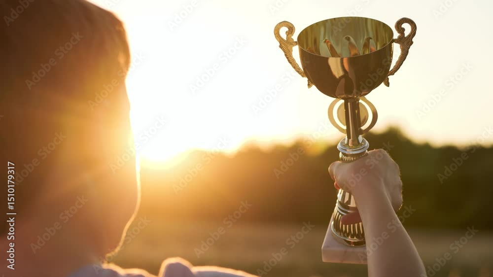 Small victor grips polished chalice against glowing horizon in vivid child victory. Bright silhouette lifts shining cup echoing kid triumph. Soft sunset beams infuse inspiring atmosphere child triumph