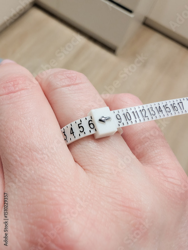 Hand holding measuring tape for ring size measurement on finger.