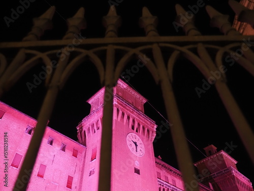 Ferrara Castle, a city in Northern Italy. Photo taken in the evening, with the castle lit up in pink behind the moat gate.