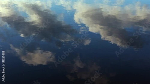 Abstract View Of Blue Sky And White And Dark Clouds Reflected On The Gently Rippling Surface Of Calm Water. Peaceful And Serene Natural Background.