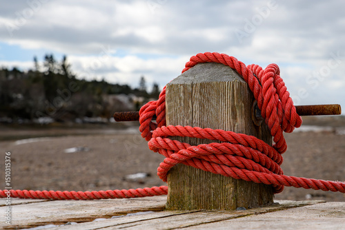Red rope tied around a post on a wooden wharf. Low tide, beach in the background. Overcast sky.