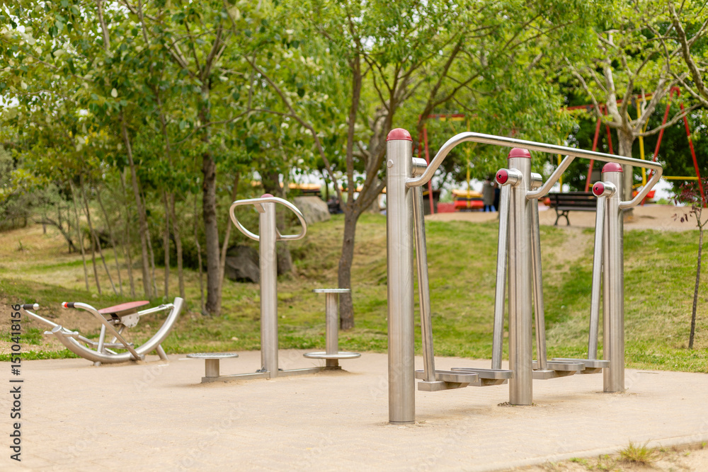 A well-maintained outdoor fitness area features multiple exercise stations designed for public use. The greenery surrounds the equipment, inviting community fitness activities A well-maintained outdoor fitness area features multiple exercise stations designed for public use. The greenery surrounds the equipment, inviting community fitness activities