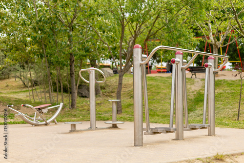 Fototapeta Naklejka Na Ścianę i Meble -  A well-maintained outdoor fitness area features multiple exercise stations designed for public use. The greenery surrounds the equipment, inviting community fitness activities